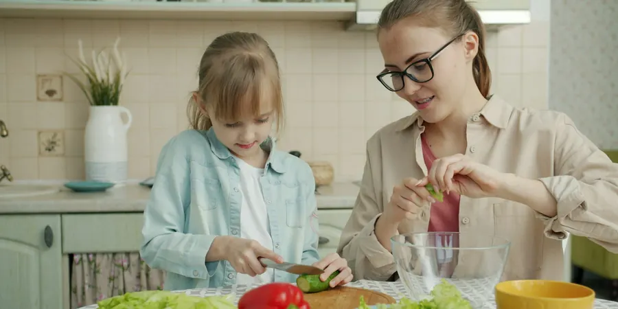 Mãe e filha preparando salada na cozinha, alimentação que ajuda contra o colesterol alto em criança