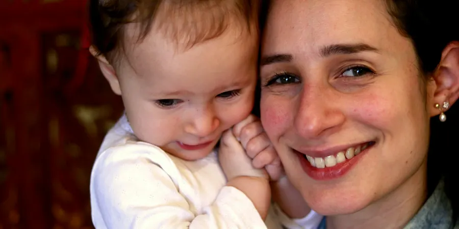 Mãe sorridente com a filha bebê no colo, família que acompanha a comunicação interatrial (CIA)