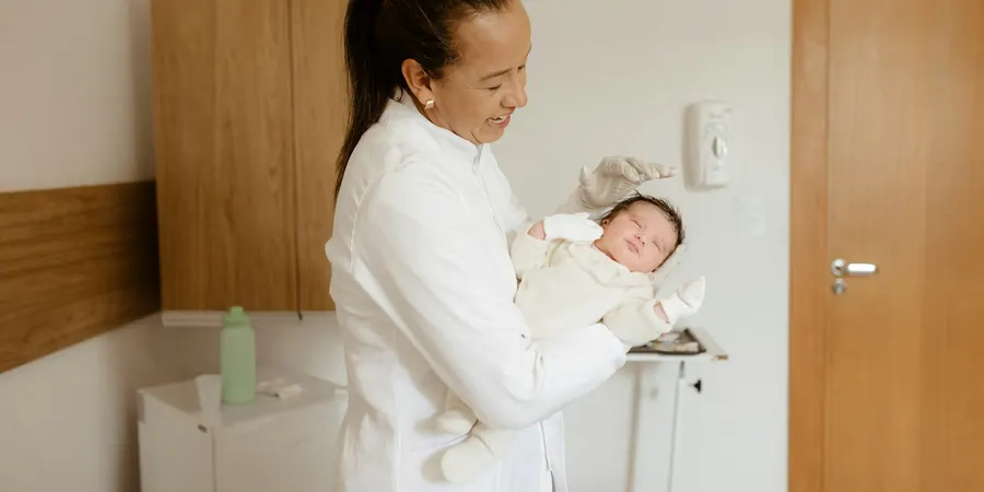 Pediatra sorrindo com um recém-nascido no colo no consultório, acompanhamento da comunicação interventricular (CIV)