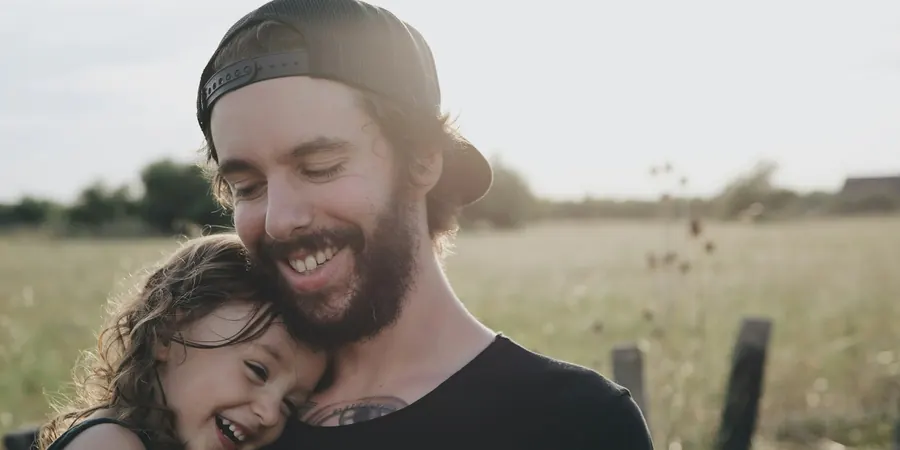 Pai e filha abraçados e sorrindo ao ar livre, cuidado com desmaio em criança