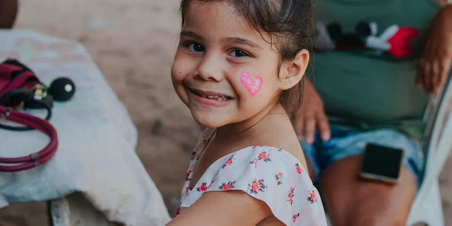 Menina sorridente com um coração pintado no rosto e estetoscópio ao lado, extrassístole em criança