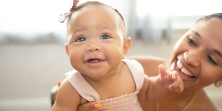 Bebê sorridente no colo da mãe em casa, acompanhamento do forame oval patente em bebê