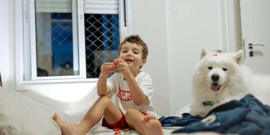 Menino brincando na cama com o cachorro, rotina normal durante o holter 24 horas em criança