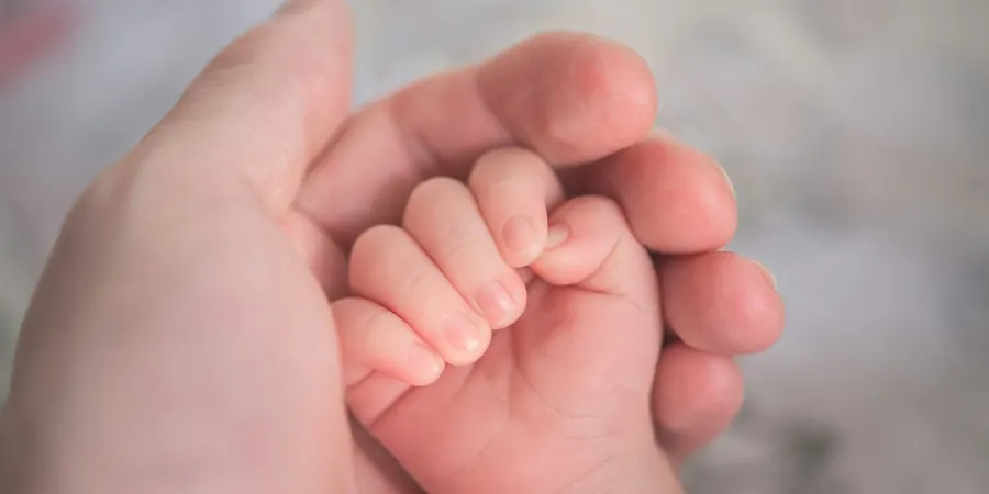 Mão de bebê segurando a mão de um adulto, cuidado com a persistência do canal arterial
