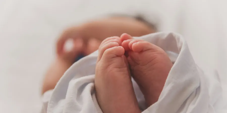 Pés de um recém-nascido enrolado em manta, fase da vida em que se faz o teste do coraçãozinho