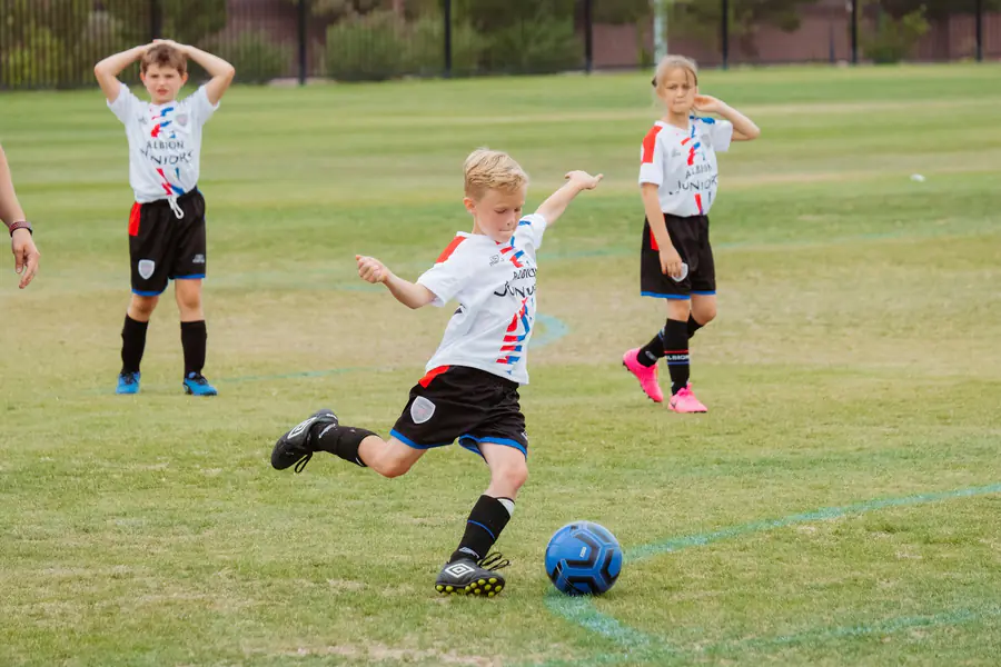 Menino chutando a bola em campo de grama durante jogo de futebol infantil, tema da avaliação cardiológica de atletas